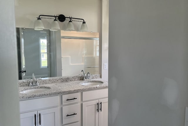 full bath featuring double vanity, a sink, and a shower with shower door