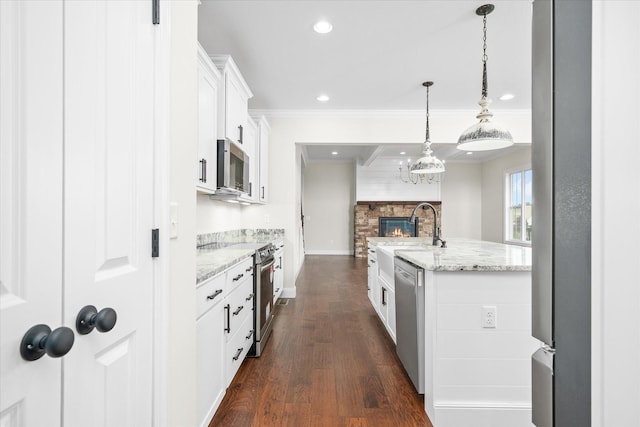 kitchen featuring white cabinetry, decorative light fixtures, ornamental molding, stainless steel appliances, and light stone countertops