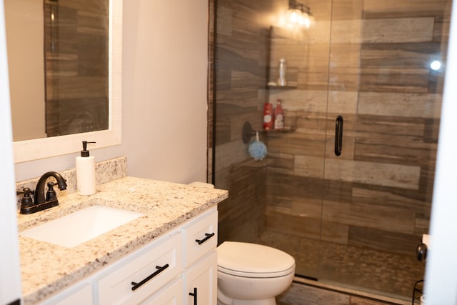 bathroom featuring a shower with shower door, toilet, and vanity