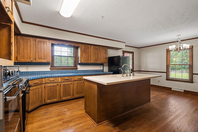 kitchen featuring an inviting chandelier, hanging light fixtures, black refrigerator, hardwood / wood-style floors, and a kitchen island with sink