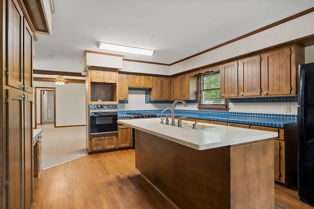 kitchen with sink, backsplash, a kitchen island with sink, black appliances, and light hardwood / wood-style flooring