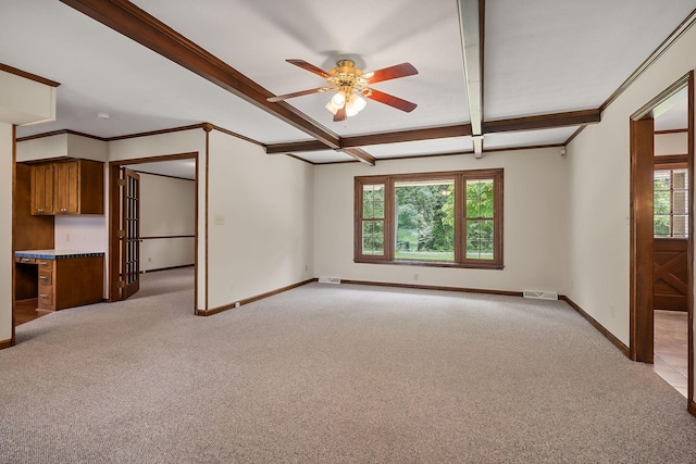 unfurnished living room featuring a healthy amount of sunlight, built in desk, light colored carpet, and beam ceiling