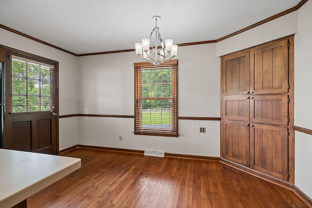 unfurnished dining area with dark wood-type flooring, crown molding, and an inviting chandelier