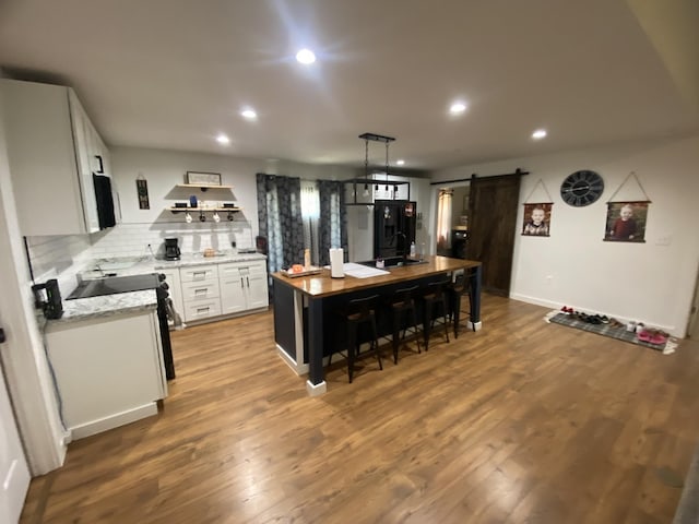 kitchen with white cabinetry, a center island, light hardwood / wood-style flooring, black refrigerator, and a barn door