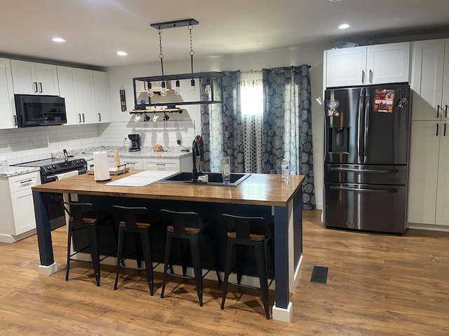 kitchen featuring white cabinetry, black fridge with ice dispenser, butcher block countertops, and a center island with sink