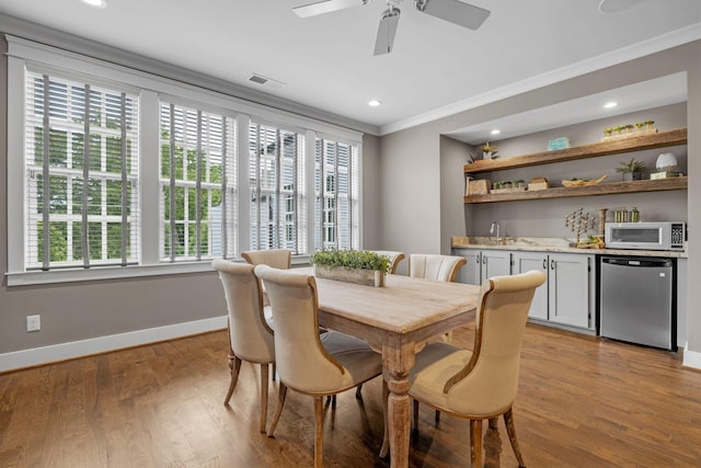 dining area with crown molding, ceiling fan, bar area, and light wood-type flooring