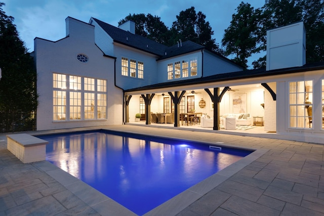 pool at dusk with ceiling fan, outdoor lounge area, and a patio