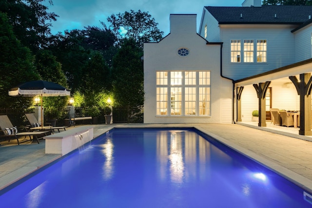 pool at dusk featuring a patio, pool water feature, and french doors