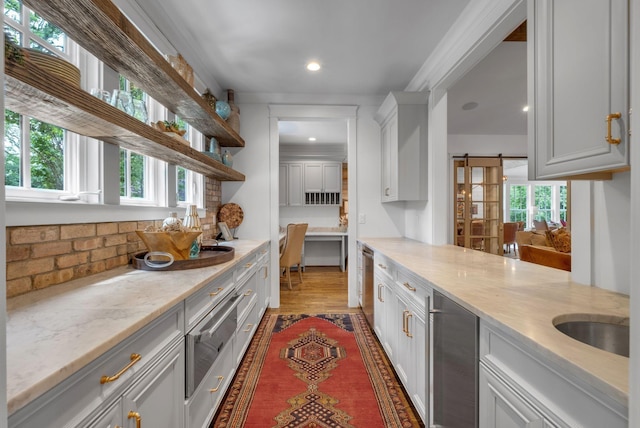 kitchen with white cabinetry, sink, light stone counters, a barn door, and a healthy amount of sunlight