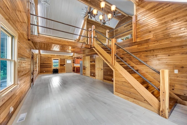 unfurnished living room with wood-type flooring, wooden walls, a chandelier, and high vaulted ceiling