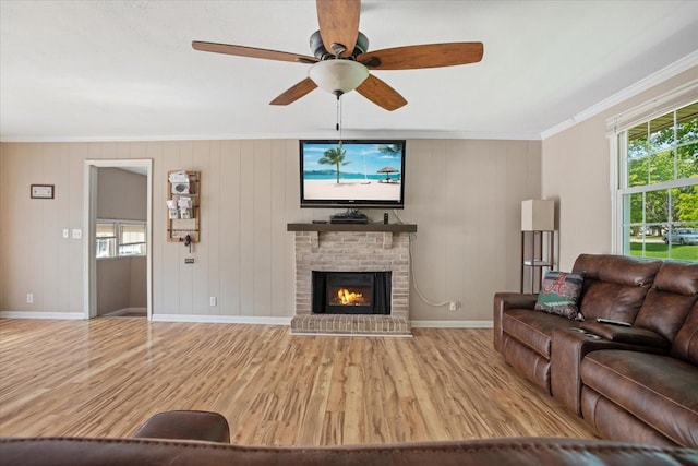 living room featuring a brick fireplace, light hardwood / wood-style flooring, ornamental molding, and ceiling fan