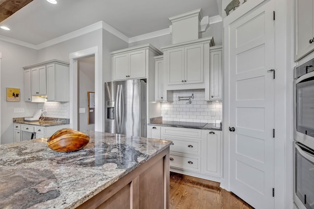 kitchen with light stone counters, backsplash, white cabinetry, and appliances with stainless steel finishes