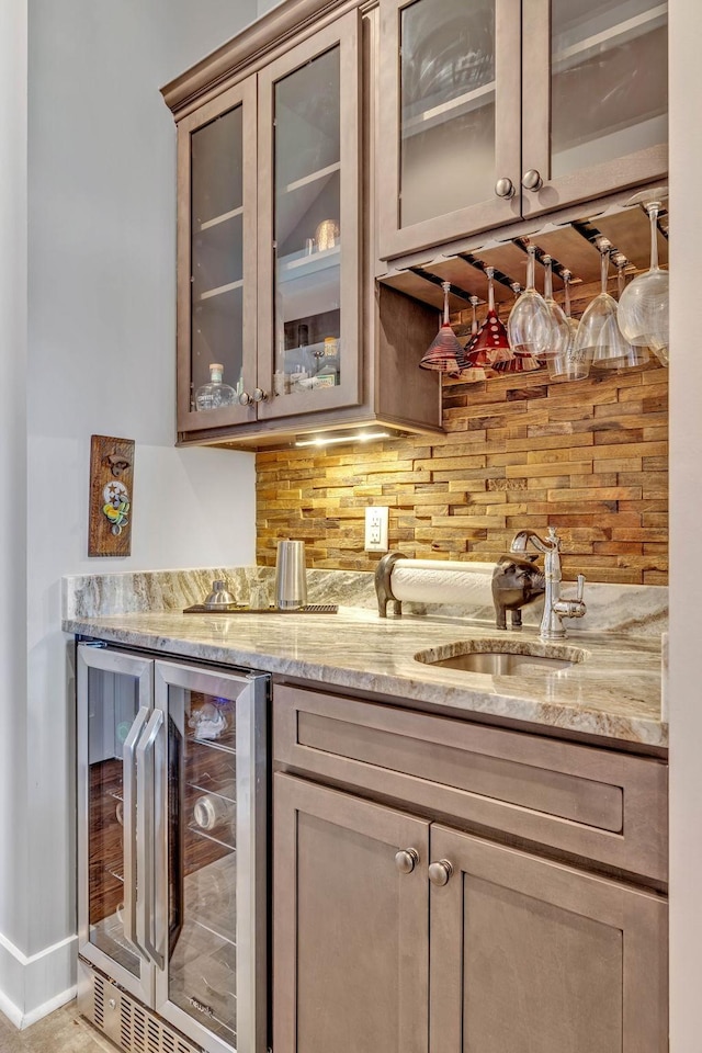 bar featuring wine cooler, sink, tasteful backsplash, and light stone countertops