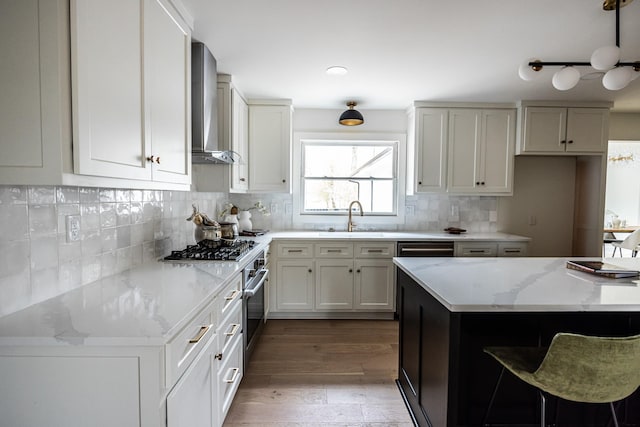 kitchen featuring white cabinets, wall chimney exhaust hood, appliances with stainless steel finishes, light stone countertops, and a sink