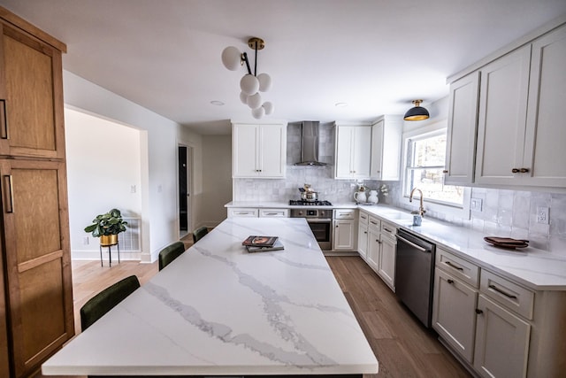 kitchen featuring stainless steel appliances, a spacious island, white cabinetry, wall chimney exhaust hood, and decorative light fixtures