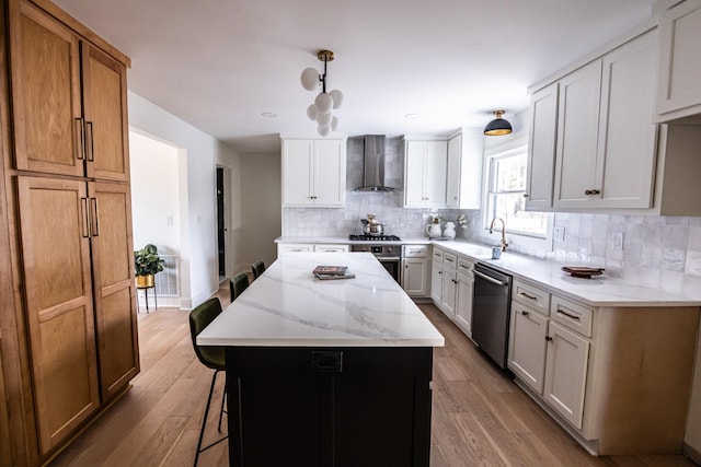 kitchen with a center island, decorative light fixtures, appliances with stainless steel finishes, white cabinetry, and wall chimney exhaust hood