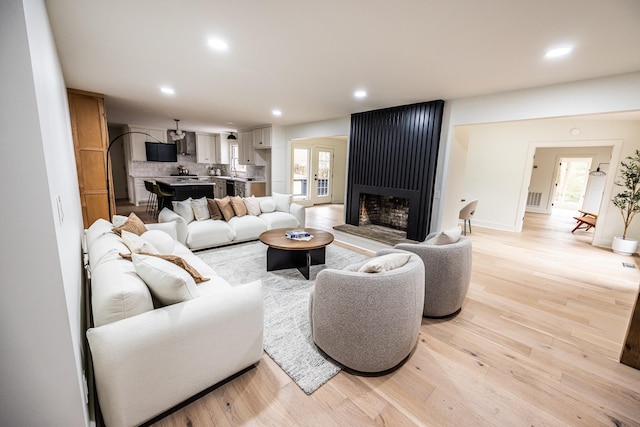 living room featuring recessed lighting, a fireplace, baseboards, light wood-style floors, and french doors