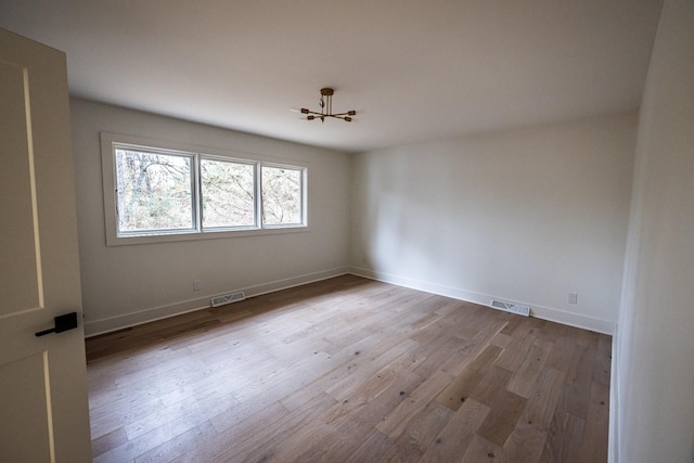 empty room with visible vents, light wood-style flooring, and baseboards