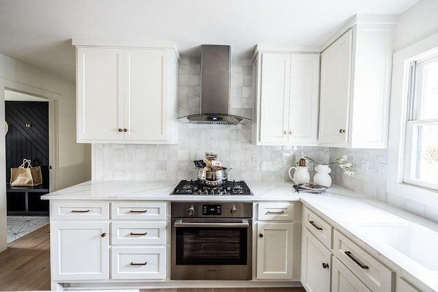 kitchen featuring appliances with stainless steel finishes, white cabinetry, decorative backsplash, and wall chimney exhaust hood