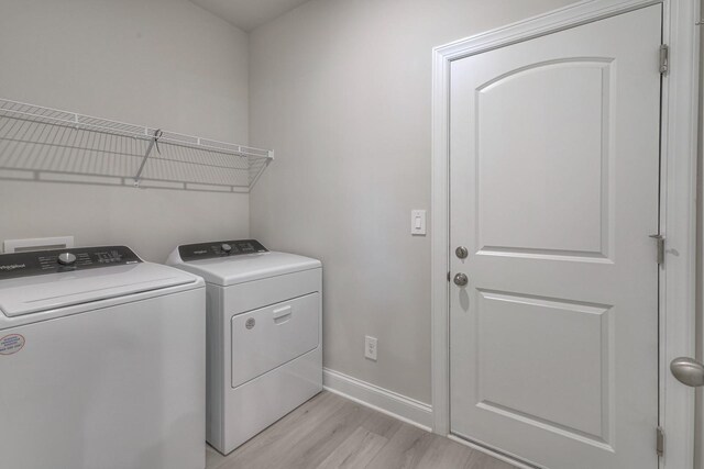 laundry room with washing machine and clothes dryer and light hardwood / wood-style floors