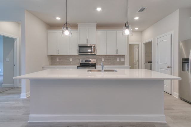 kitchen featuring hanging light fixtures, stainless steel appliances, sink, and a center island with sink