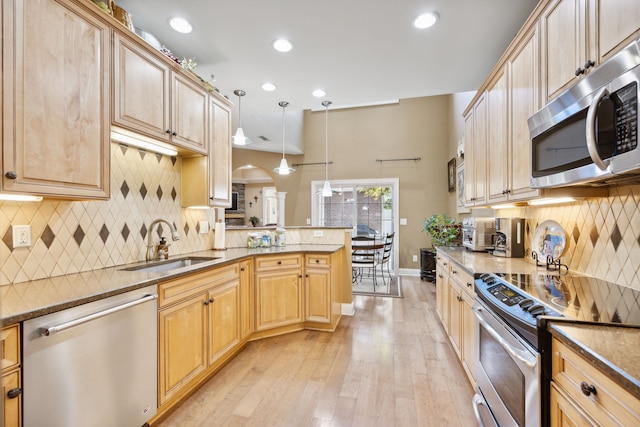 kitchen with tasteful backsplash, light hardwood / wood-style floors, pendant lighting, kitchen peninsula, and appliances with stainless steel finishes