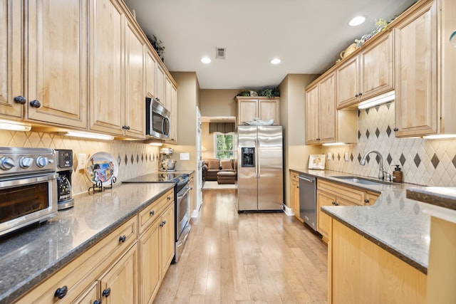 kitchen with light hardwood / wood-style floors, light brown cabinetry, dark stone countertops, sink, and appliances with stainless steel finishes