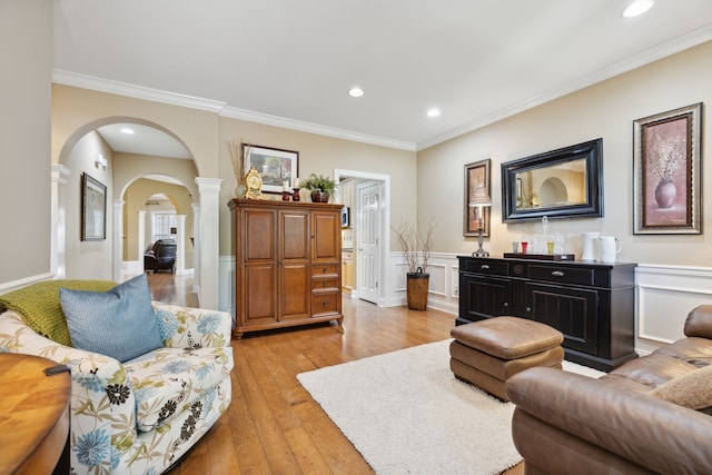 living room with decorative columns, crown molding, and light hardwood / wood-style flooring