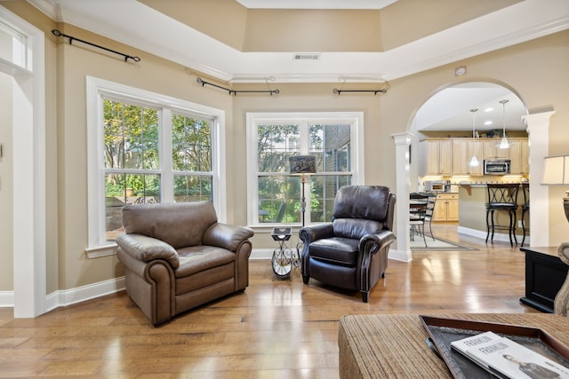 living room featuring light wood-type flooring, crown molding, and decorative columns