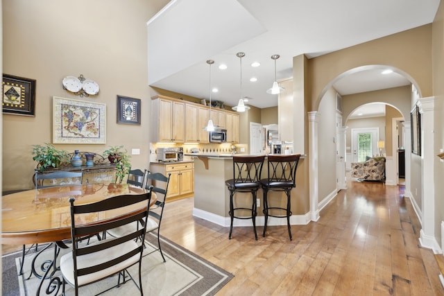 dining space featuring a high ceiling, light wood-type flooring, and decorative columns