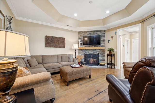 living room with crown molding, a stone fireplace, light hardwood / wood-style floors, and a raised ceiling