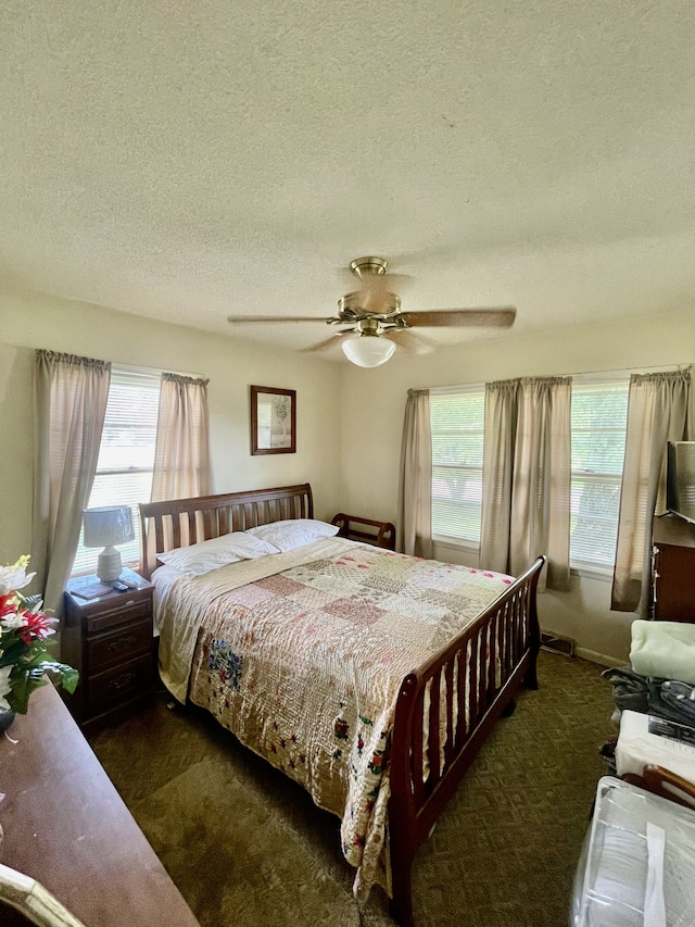 bedroom featuring a textured ceiling, multiple windows, ceiling fan, and dark carpet