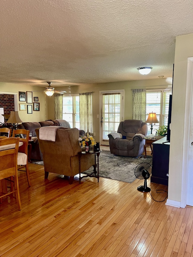 living room featuring ceiling fan, plenty of natural light, light hardwood / wood-style flooring, and a textured ceiling