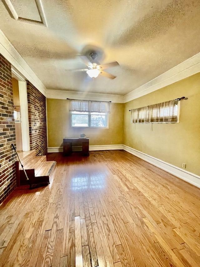 interior space featuring hardwood / wood-style floors, a textured ceiling, ceiling fan, and brick wall