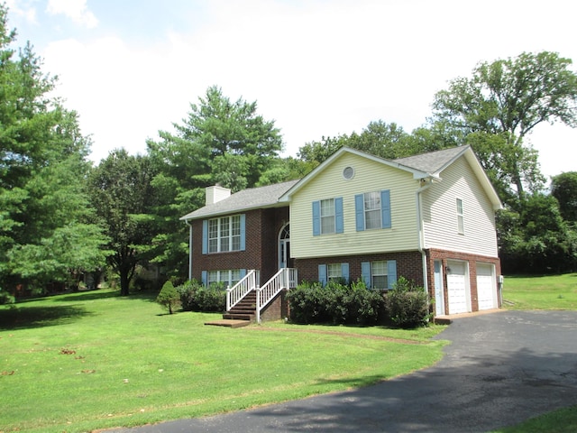 raised ranch with brick siding, a chimney, a front yard, a garage, and driveway