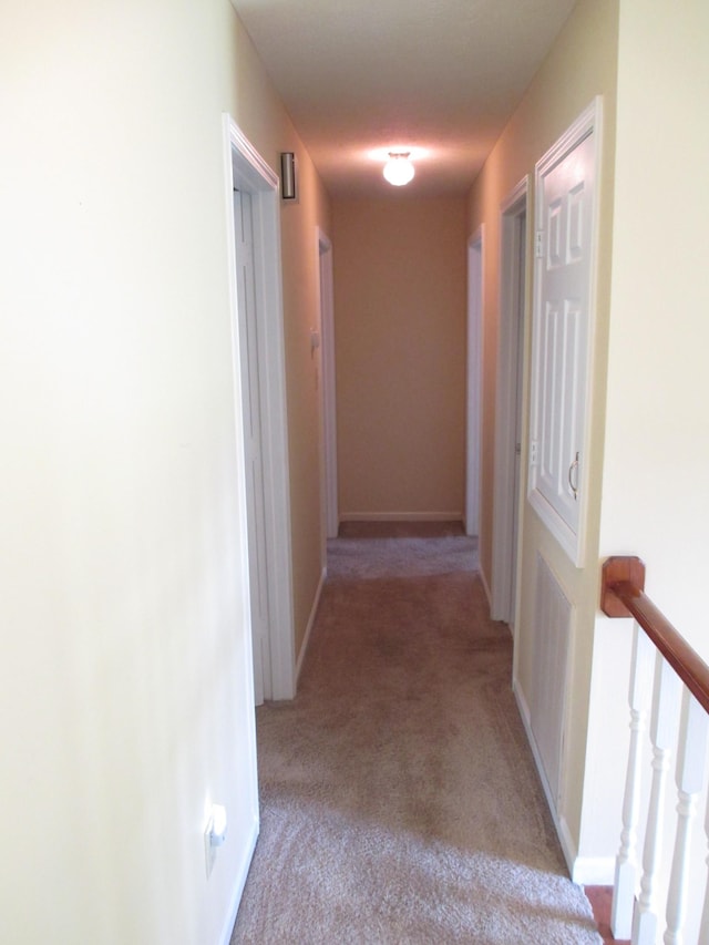 hallway featuring light colored carpet and baseboards