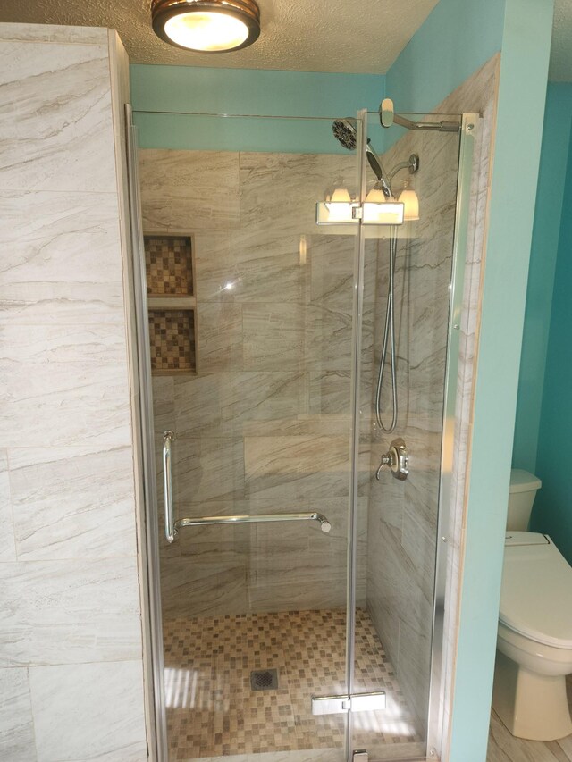 bathroom with a textured ceiling, toilet, and walk in shower