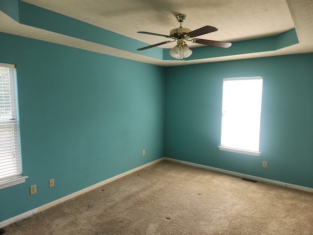 carpeted empty room with ceiling fan, a healthy amount of sunlight, a raised ceiling, and a textured ceiling