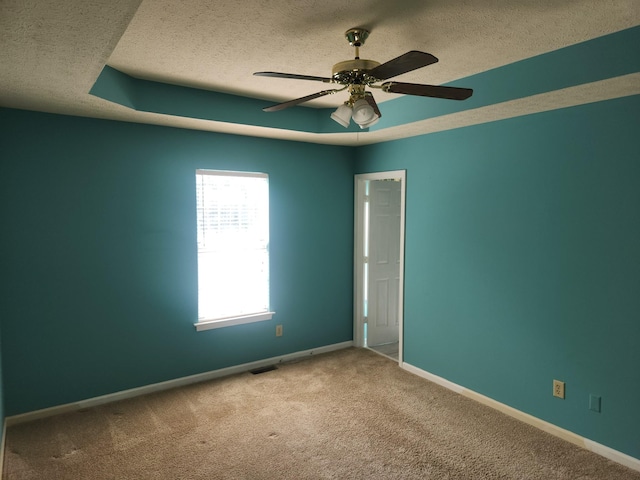 empty room featuring a textured ceiling, a tray ceiling, carpet flooring, and baseboards