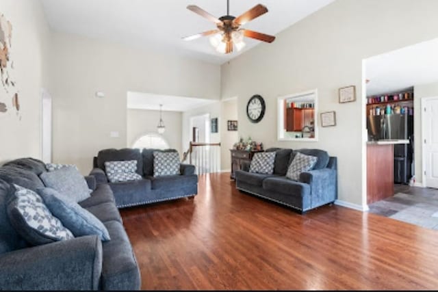 living room with dark wood-type flooring, ceiling fan, and a high ceiling