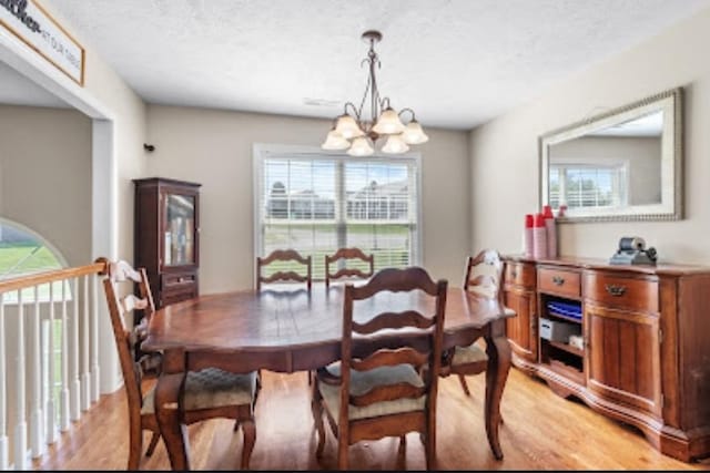 dining space featuring an inviting chandelier, light hardwood / wood-style floors, and a textured ceiling