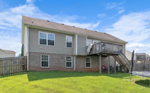 rear view of house featuring a wooden deck, a trampoline, and a lawn