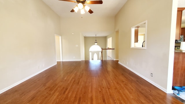 unfurnished living room featuring hardwood / wood-style flooring, ceiling fan, and a high ceiling