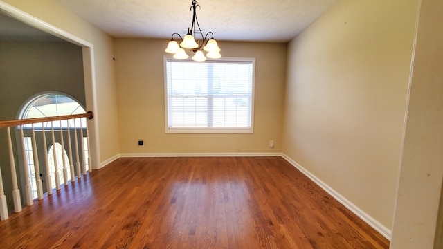 empty room with dark hardwood / wood-style flooring, a chandelier, a textured ceiling, and a wealth of natural light