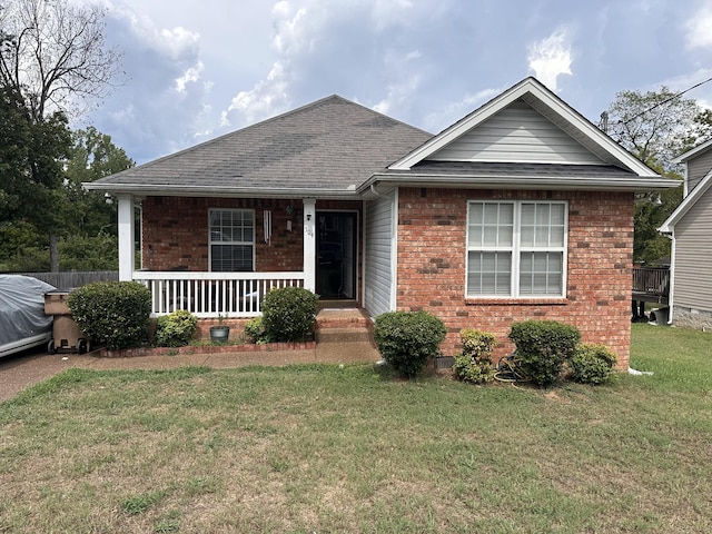 view of front of property featuring covered porch, roof with shingles, a front yard, and brick siding