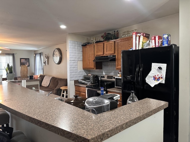 kitchen featuring a breakfast bar area, under cabinet range hood, electric range, black fridge with ice dispenser, and open floor plan