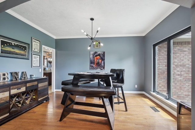 dining space with a notable chandelier, ornamental molding, a textured ceiling, and light wood-type flooring