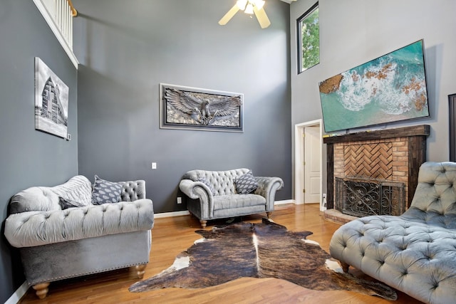 sitting room with hardwood / wood-style floors, a high ceiling, a brick fireplace, and ceiling fan