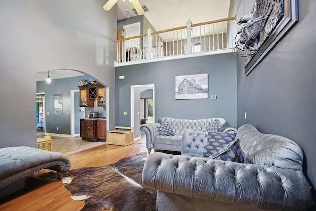 living room with ceiling fan, light hardwood / wood-style flooring, and a towering ceiling