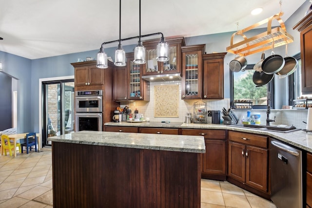 kitchen featuring pendant lighting, decorative backsplash, a center island, stainless steel appliances, and light stone countertops